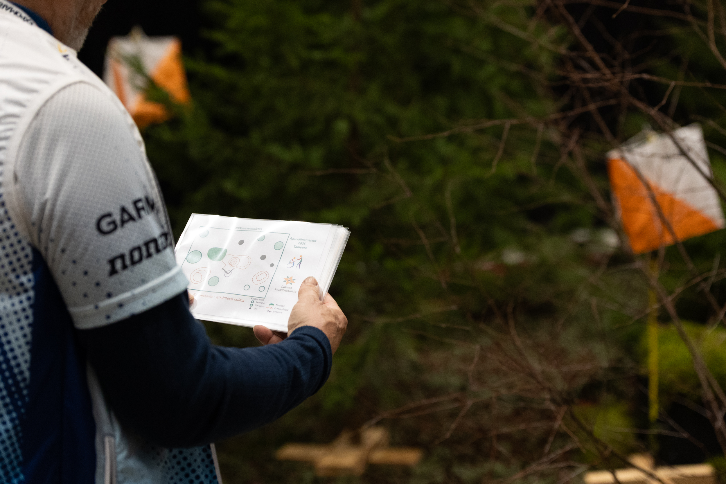 Kuvassa henkilö lukee suunnistuskarttaa ja taustalla näkyy rastilippu.